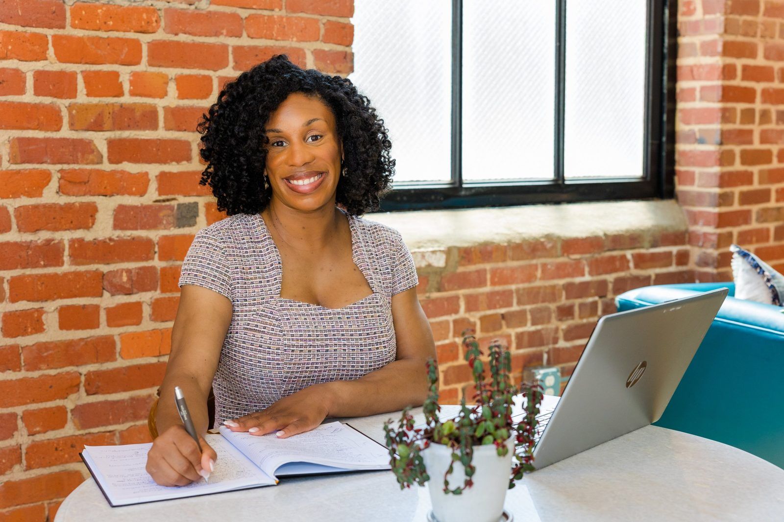 Cassandra Davis, founder of CDavis Enterprises, writing at a table by a brick wall